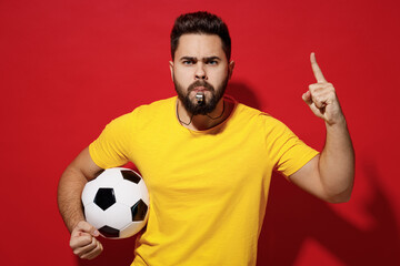 Young bearded man football trainer in yellow t-shirt whistle hold soccer ball keep one finger...