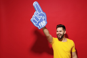 Smiling excited overjoyed young bearded man 20s in yellow t-shirt cheer up support favorite sport...