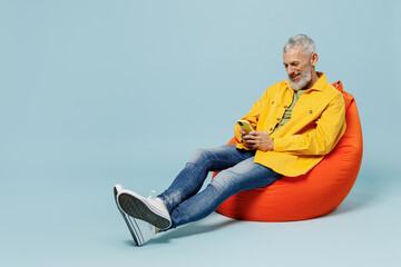 Full body smiling happy elderly gray-haired mustache bearded man 50s in yellow shirt sit in bag...