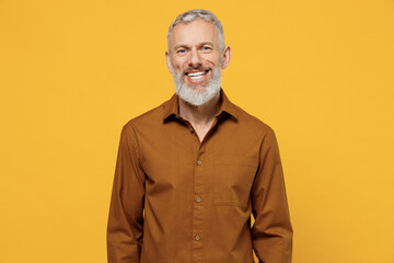 Happy excited magnificent elderly gray-haired bearded man 40s years old wears brown shirt looking camera smiling isolated on plain yellow background studio portrait. People emotions lifestyle concept.