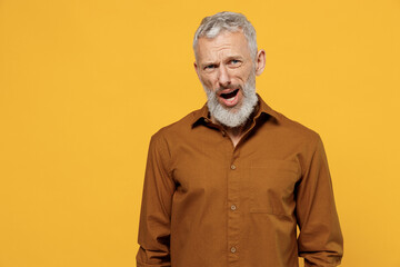 Sceptical elderly gray-haired bearded man 40s years old wears brown shirt looking camera keeping mouth wide open isolated on plain yellow background studio portrait. People emotions lifestyle concept.