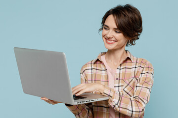 Young smiling happy copywriter woman 20s wearing casual brown shirt hold use work on laptop pc computer isolated on pastel plain light blue color background studio portrait. People lifestyle concept.