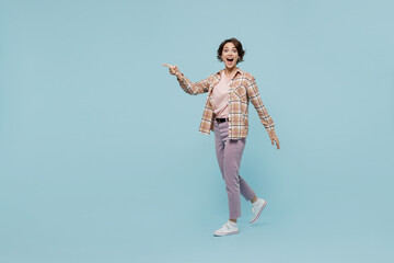 Full body side view young smiling happy woman 20s wearing casual brown shirt walking go point index finger aside on workspace area isolated on pastel plain light blue color background studio portrait