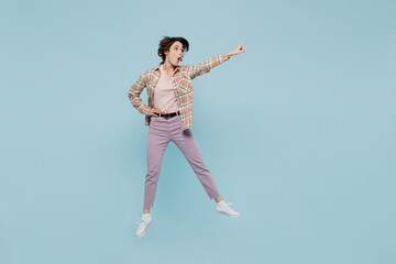 Full body young excited amazed woman 20s wearing casual brown shirt jump high point index finger aside on workspace area mock up isolated on pastel plain light blue color background studio portrait