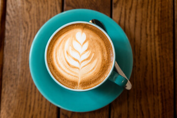 Latte art leaf in coffee cup on wooden table top view.