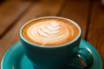 Latte art leaf in coffee cup on wooden table side view