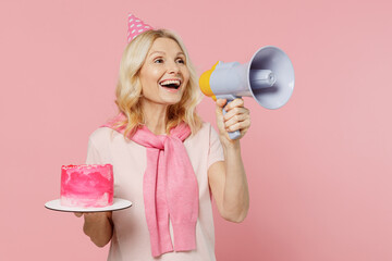 Elderly happy woman 50s in t-shirt birthday hat hold cake hold scream in megaphone announces...