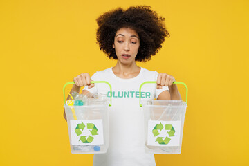 Young serious woman of African American ethnicity wears white volunteer t-shirt hold boxes for waste sorting isolated on plain yellow background. Voluntary free work assistance help charity concept.