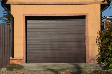A close-up of a detached car garage with rolling automatic garage door, roof gutters and a downpipe.