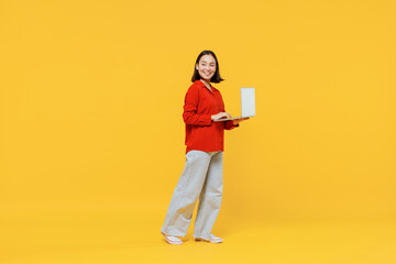 Full size body length vivid smiling happy young woman of Asian ethnicity 20s years old in casual clothes look back hold laptop pc computer go move isolated on plain yellow background studio portrait.