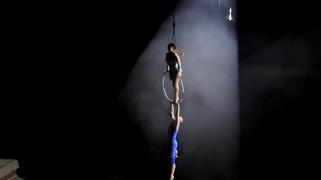 Aerial acrobat on the circus stage. A young girl and a guy perform acrobatic elements on the air ring, in the circus arena. Circus artists create shows for the audience. Flexible, athletic, aerialists