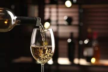 Fotobehang Pouring white wine from bottle into glass on blurred background, closeup. Space for text © New Africa