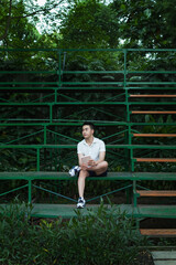 Male student with white shirt, blue short is studying in green park