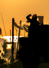 Pécheur qui tire son filet de pêche dans le coucher de soleil.