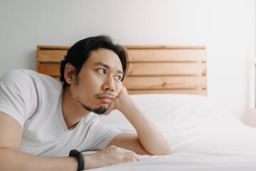 Exhausted Asian man lay on the bed as he feels burnout.