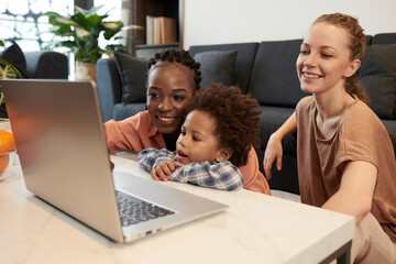 Diverse lesbian couple and little son watching animated cartoon on laptop at home