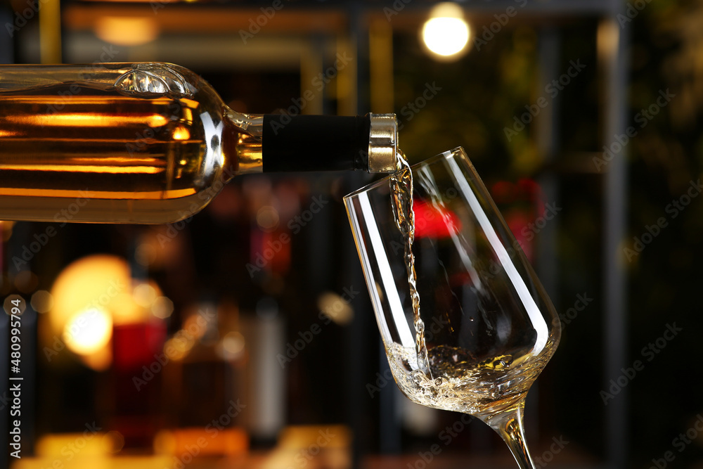 Poster Pouring white wine from bottle into glass on blurred background, closeup