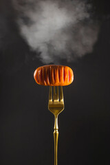 Delicious hot grilled meat sausage with smoke on a golden fork on a black background. Vertical image with copy space