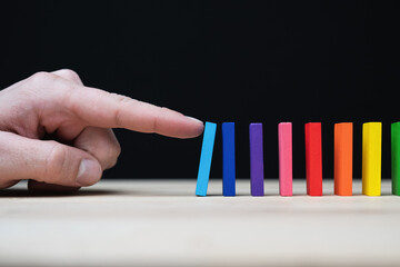 Conceptual photo of a hand starting a chain reaction with colored dominoes.
Domino effect with...