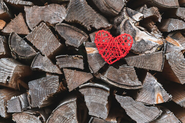 A braided red heart in front of a pile of wood. Lots of copyspace in the photo. 
