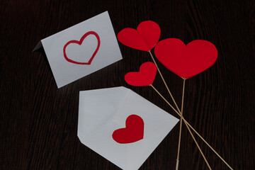 A white envelope with a red heart, a love message and flags in the form of red cardboard hearts. Attributes of Valentine's day, on a brown, textured background, with a wood texture.