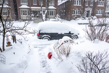 Fototapeta premium As a blizzard sweeps into a residential neighbourhood the streets fill with snow and residents start to shovel out their cars and sidewalks. Shot in Toronto’s Beaches neighbourhood in January.