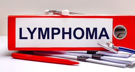 On the desktop is a stethoscope, documents, a pen, and a red file folder with the text LYMPHOMA. Medical concept