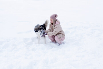 Fototapeta na wymiar Young woman playing with siberian husky dog in the snow on winter day, training and walking her pet dog. Friendship, lovely dog, best pet, dog for a walk with his owner