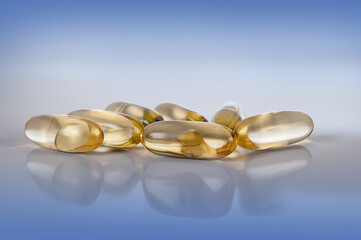 yellow vitamin e fish oil capsule on light blue background with reflection close up