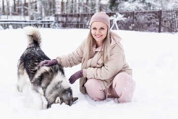 Young woman playing with siberian husky dog in the snow on winter day, training and walking her pet dog. Friendship, lovely dog, best pet, dog for a walk with his owner