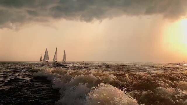 A few sailboats in a sea at sunset, magic sun reflection, sun path, the sky of pink color, the darkness storm sky, rain cloud in horizon, calm dark water