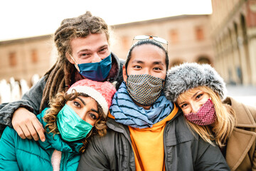 Multicultural friends taking selfie wearing face mask on winter clothes - New normal life style concept with young people having fun together outdoors - Warm vivid filter