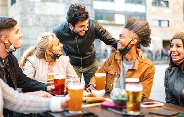 Young friends drinking beer with open face mask - New normal life style concept with trendy people having fun together on happy hour at outside brewery bar - Warm filter with focus on central guy
