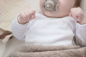 baby in white clothes lying in bed with cute pacifier