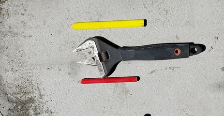 Plumbing repair tools and two simple pencils in red and yellow on a concrete background.