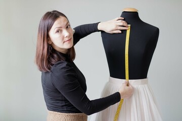 Woman designer measures with measuring tape the distance to the waist on a mannequin. The white skirt is on the mannequin