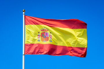 The national flag of Spain is flying in the wind at full mast against blue sky.