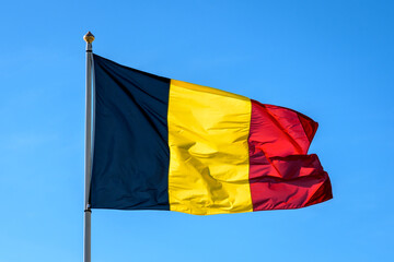 The national flag of Belgium is flying in the wind at full mast against blue sky.