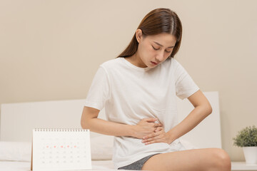 Menstruation, period cycle day of monthly, hurt asian young woman, female hand in stomachache, suffer from PMS premenstrual, belly or abdomen pain on bed at home. Health problem Inflammation in body - obrazy, fototapety, plakaty