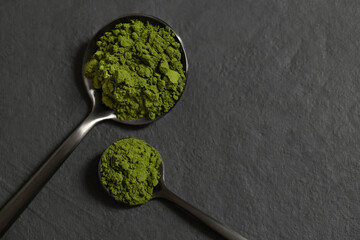 Chlorella green powder in spoons on a black stone background. Spirulina powder algae or barley. Superfood. Copy space, top view, flat lay.