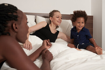 Boy with strabismus sitting in bed with his two mothers and watching movie or animated cartoon