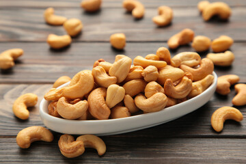 Cashew nuts on white plate on brown wooden background. Top view.