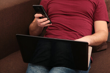 Young man working at home using laptop and smartphone