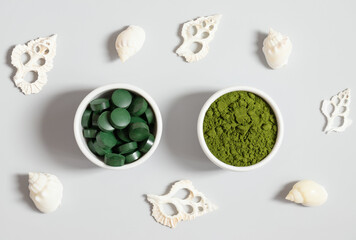 Chlorella and spirulina on a gray background with seashells. Chlorella powder and spirulina tablets. Detox superfood. Natural supplement of algae. View from above.
