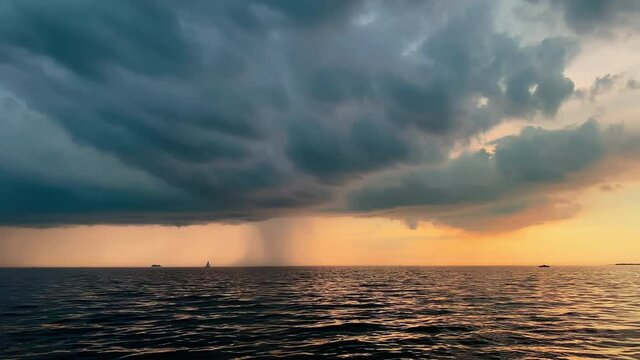 The lonely sailboat in a list goes by sea at sunset, the sky of pink color, the darkness storm sky, rain cloud in horizon, calm water, magic sun reflection, sun path