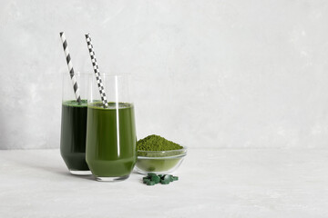 Chlorella and spirulina green detox drinks. Chlorella powder and spirulina tablets, glasses with green drinks on a gray background. Superfood concept. Space for text.