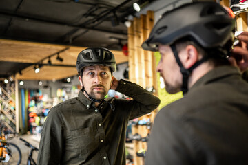 Young man came to the bicycle store. He is measuring the helmet. Male chooses helmet in sports equipment store. Purchase of new sports helmet. Customer with bicycle helmet trying on near the mirror