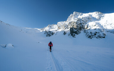 Fototapeta na wymiar A skier is walking up the hill. Skitouring in Alps. Sunny weather. Adventure winter sport
