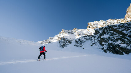 Naklejka na ściany i meble A skier is walking up the hill. Skitouring in Alps. Sunny weather. Adventure winter sport