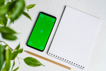 Green leave with blank notepad smartphone green screen mockup and pencil flat lay. Top view